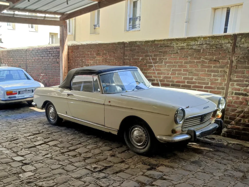 Peugeot 404 Cabriolet blanc cassé devant mur de brique